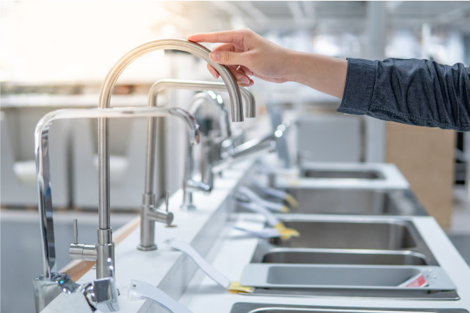 A man is reaching out and touching a kitchen faucet on display in a home improvement store