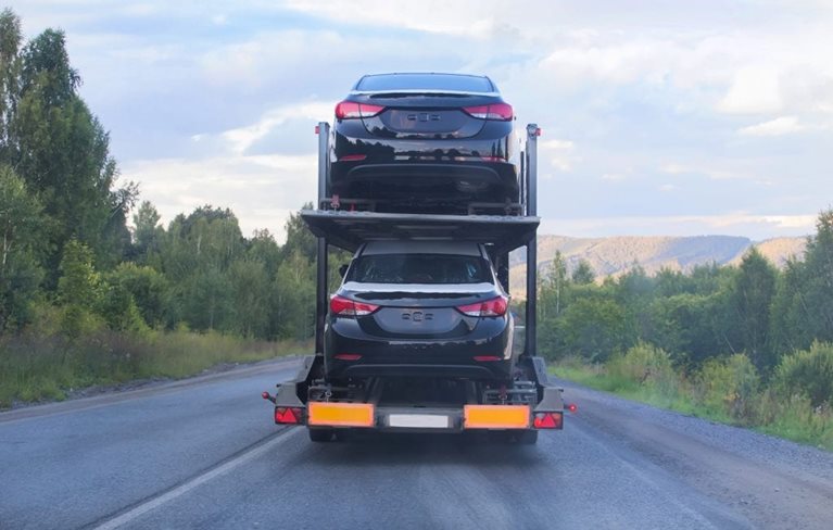 Rear view of a vehicle shipping carrier truck as it travels cross-country through a remote, forested part of the country.