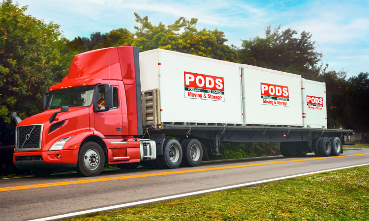 A PODS truck is transporting three PODS portable moving and storage containers along a remote freeway.
