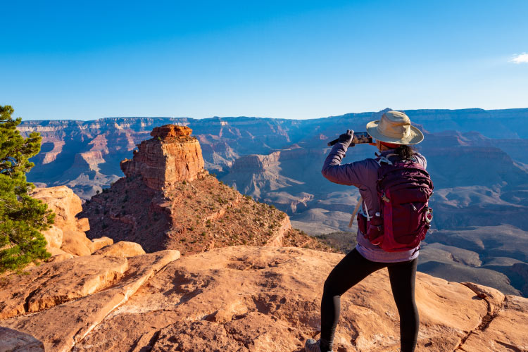 A woman in hiking gear is taking a photo of the Grand Canyon from the South Rim in Arizona.