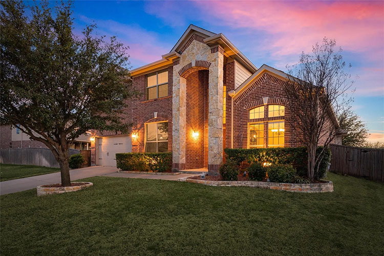 A brick, multi-story home in Roanoke, Texas. There are multiple windows and a garage door. To the left is the driveway and to the right is the green lawn. 