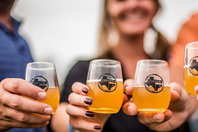Four friends hold their craft beer tasting glasses together for a photo at a food and wine fair in Cypress, Texas.