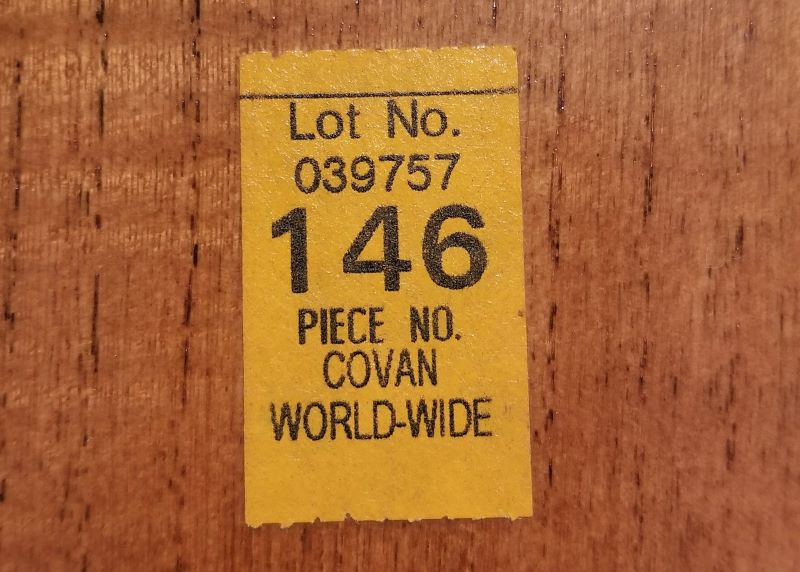 A close-up view of a yellow tracking sticker used for military PCS moves stuck to a piece of wooden furniture.