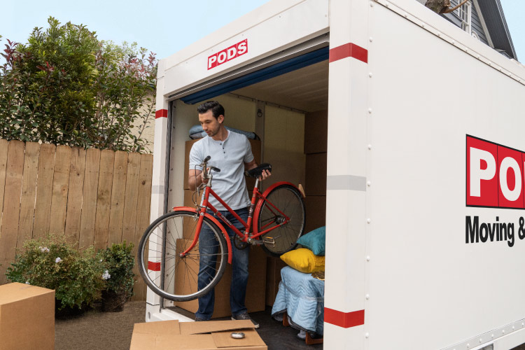 A man is carrying a bicycle out of his PODS portable moving and storage container.