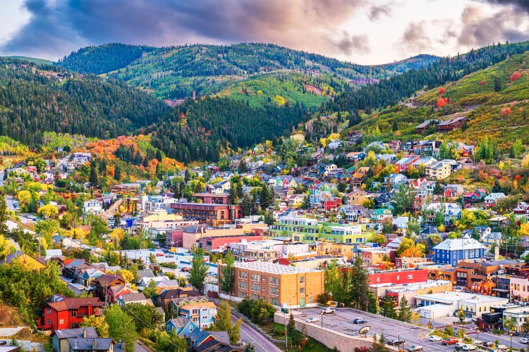 Aerial view of Park City, Utah, in early autumn. The trees and other greenery on the surrounding mountains are lush with foliage, which contrasts beautifully with the colorful buildings of this popular small town.