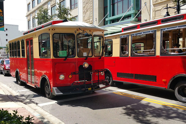 Two red trolleys pass each other on the streets of West Palm Beach. One of the trolleys has a sign in the window that reads “green line.” 