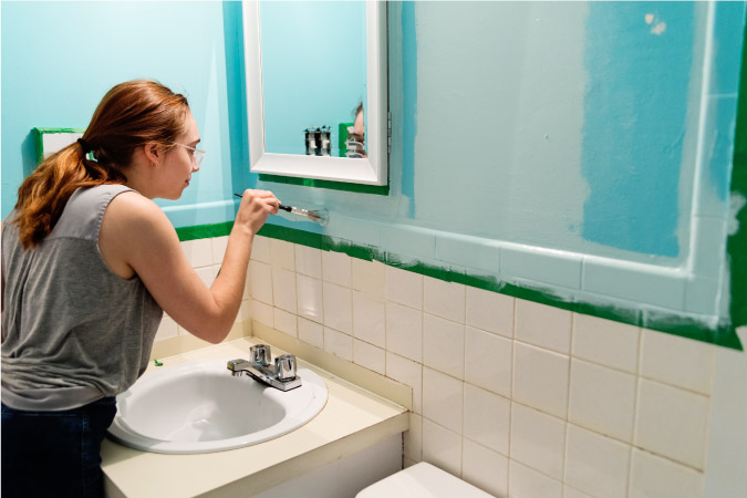 A young woman, who knows how to remodel a bathroom, is painting the walls