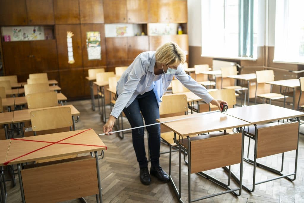Woman measuring space between desks in classroom to prepare reopening schools