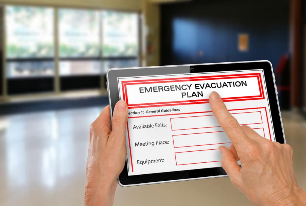 Hands holding tablet completing emergency evacuation plan near exit doors of a building