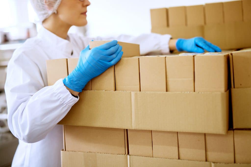 Woman handling medical supply boxes while wearing gloves and a hair net